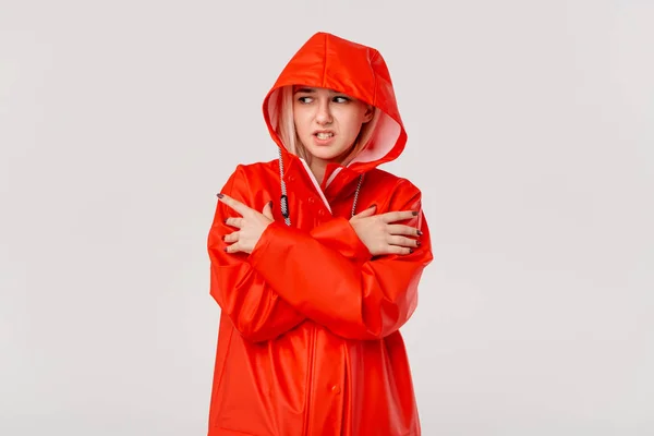 Menina loira em uma capa vermelha com um capuz está congelando de pé isolado sobre fundo branco. Você está pronto para o frio mau tempo ? — Fotografia de Stock