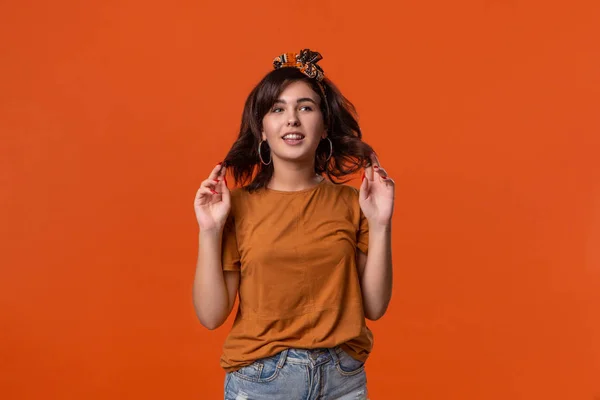 Smiling brunette woman in a t-shirt and beautiful headband standing isolated over orange background. Place for ad.