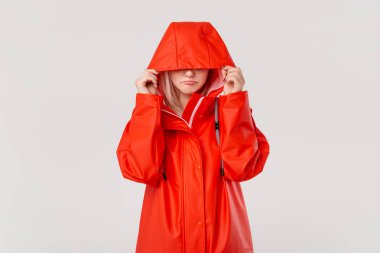 Kapüşonlu kırmızı yağmurluklu sarışın kız beyaz arka plan üzerinde izole ayakta donuyor. Soğuk kötü hava için hazır mısınız?