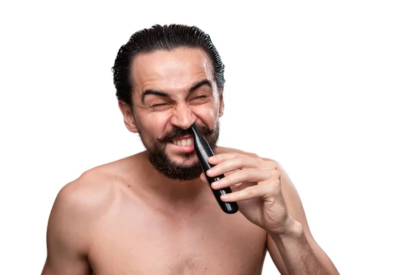 Beau barbu homme avec moustache utilise coupe-puissance pour couper les cheveux dans le nez debout nu isolé sur fond blanc. Concept de traitement matinal et de rasage . — Photo