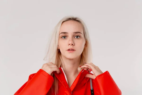 Blond girl gets on hood of a red raincoat isolated over white background. It is starting to rain. — Stock Photo, Image