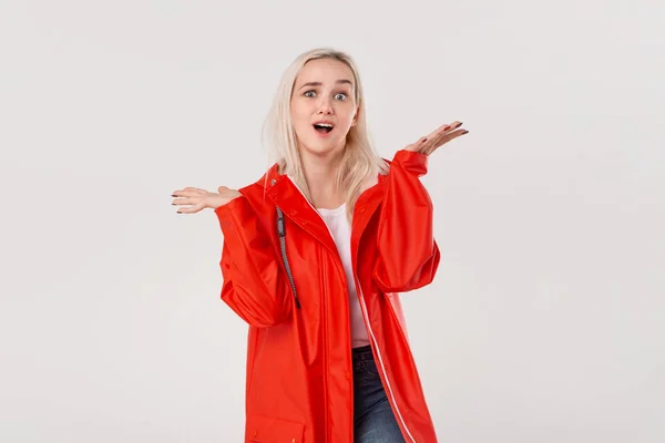 Emocionado chica rubia bonita en un impermeable rojo y camiseta blanca de pie aislado sobre fondo blanco. El mal tiempo no significa mal humor. . —  Fotos de Stock