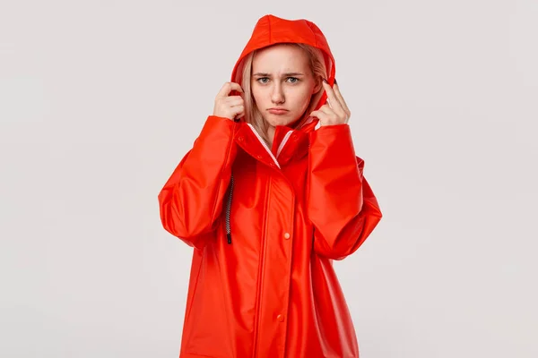 Chica rubia en un impermeable rojo con una capucha se está congelando de pie aislado sobre fondo blanco. ¿Estás listo para el mal tiempo frío ? —  Fotos de Stock