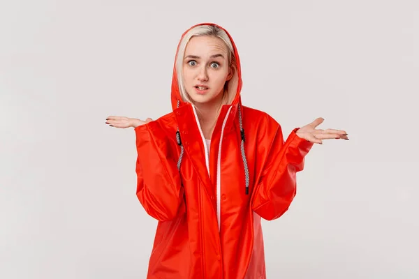 Chica rubia en un impermeable rojo con capucha expresando emoción de indignación debido al clima lluvioso aislado sobre fondo blanco. Prepárate para el mal tiempo . —  Fotos de Stock