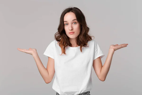 O gri arka plan üzerinde izole ayakta öfkeli ayakta o zaman omuzlarını silkme beyaz bir tee Pretty esmer kadın. Reklam alanını kopyalama.
