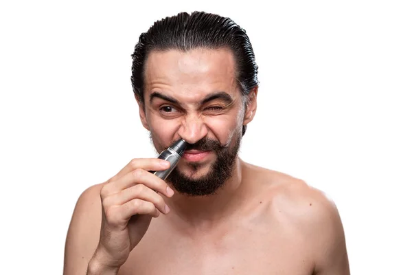 Handsome bearded man with mustache uses power trimmer to trim hair in the nose standning bare isolated over white background. Concept of morning routine and shaving. — Stock Photo, Image