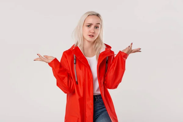 Chica rubia en un impermeable rojo con capucha expresando emoción de indignación debido al clima lluvioso aislado sobre fondo blanco. Prepárate para el mal tiempo . — Foto de Stock