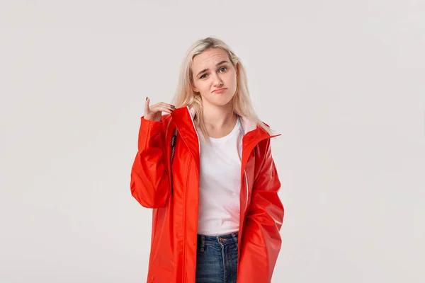 Chica rubia en un impermeable rojo con capucha expresando emoción de aversión debido al clima lluvioso aislado sobre fondo blanco. Prepárate para el mal tiempo . —  Fotos de Stock