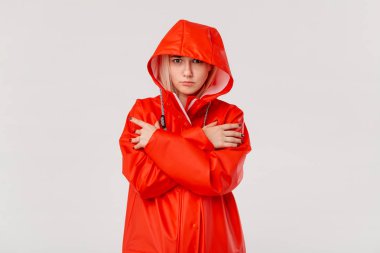 Kapüşonlu kırmızı yağmurluklu sarışın kız beyaz arka plan üzerinde izole ayakta donuyor. Soğuk kötü hava için hazır mısınız?