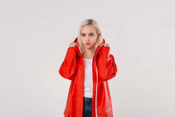 Chica rubia se pone en la capucha de un impermeable rojo aislado sobre fondo blanco. Está empezando a llover. . — Foto de Stock