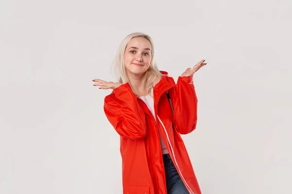 Emocionado chica rubia bonita en un impermeable rojo y camiseta blanca de pie aislado sobre fondo blanco. El mal tiempo no significa mal humor. . — Foto de Stock