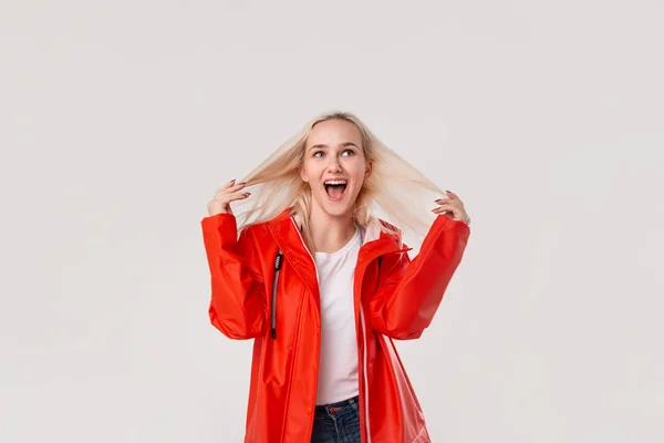 Chica rubia feliz en un impermeable rojo y camiseta blanca de pie aislado sobre fondo blanco. El mal tiempo no significa mal humor. . — Foto de Stock