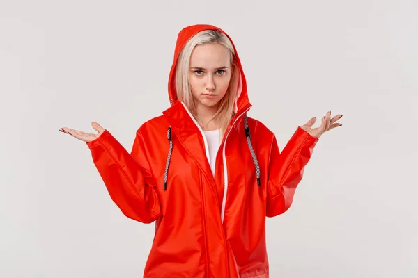 Блондинка в красном плаще с капюшоном выражает негодование из-за дождливой погоды, изолированной на белом фоне. Приготовьтесь к плохой погоде . — стоковое фото