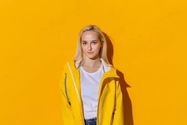 Chica rubia con un impermeable amarillo y una camiseta blanca de pie aislada sobre fondo amarillo. Ser brillante en el mal tiempo . — Foto de Stock