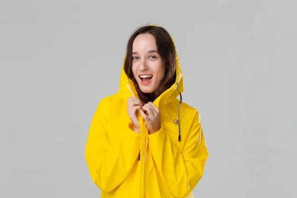 Linda chica morena con un impermeable amarillo sonriendo aislada sobre fondo gris. Prepárate para el mal tiempo . —  Fotos de Stock