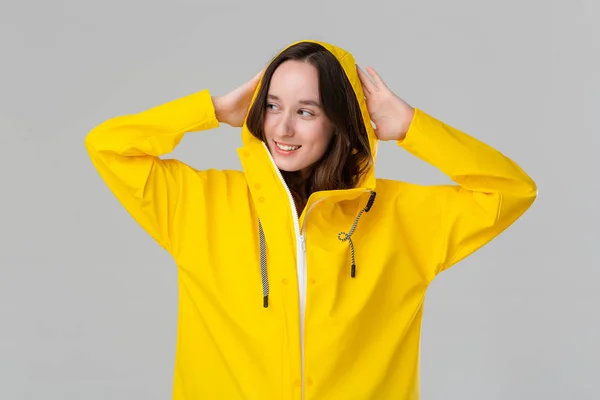 Sarı yağmurluklu güzel esmer kız gri arka planda izole bir şekilde gülümsüyor. Kötü havaya hazır ol.. — Stok fotoğraf