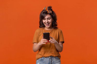 Tişörtlü, güzel saç bandı takmış güzel esmer bir kadın. Bildirimler için akıllı telefonu kontrol ediyor..