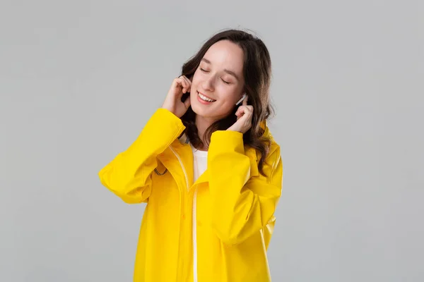 Chica morena vistiendo impermeable amarillo bailando escuchando música con auriculares inalámbricos. Concepto de disfrutar de la vida . — Foto de Stock