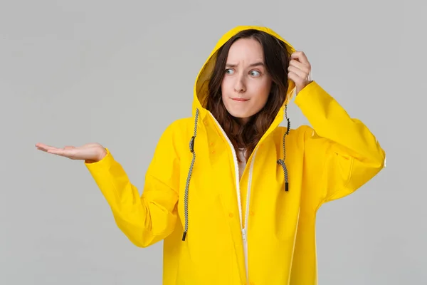 Linda chica morena en un impermeable amarillo comprobando si ha empezado a llover. Prepárate para el mal tiempo . —  Fotos de Stock