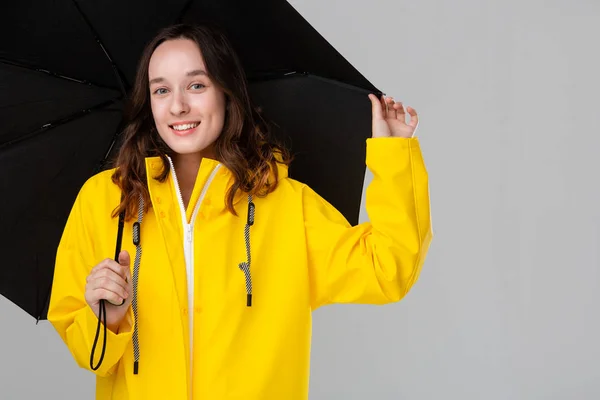 Sonriente chica morena escondida bajo paraguas negro vestida con impermeable amarillo . —  Fotos de Stock