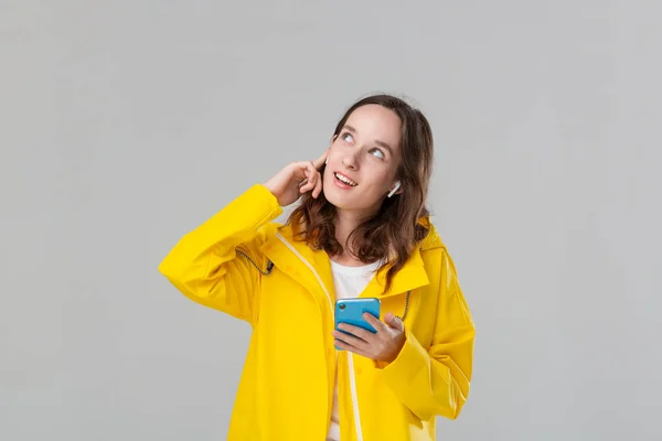 Menina morena em uma capa de chuva amarela dançando ouvir música com fones de ouvido sem fio. Conceito de desfrutar da vida . — Fotografia de Stock