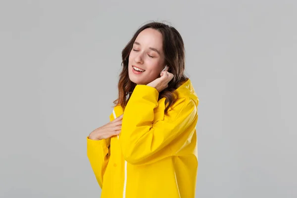 Sarı yağmurluk giyen esmer kız kablosuz kulaklıkla müzik dinliyor. Hayattan zevk alma kavramı. — Stok fotoğraf