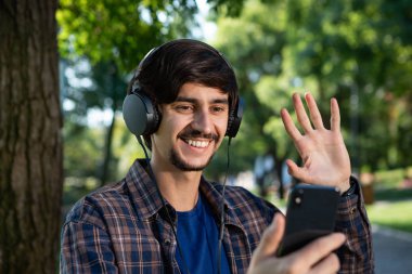 Oduncu gömlekli yakışıklı, esmer, sakallı adam müzik dinliyor ve parkta selfie çekiyor..