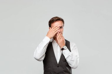 Beyaz gömlekli ve gri yelekli yakışıklı bir adam gri arka planda saklanıyor..