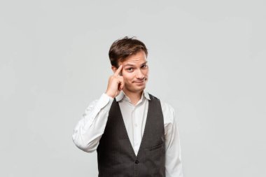 Beyaz gömlekli ve gri yelekli genç işadamı, parmağının kafasında parladığını gösteriyor..