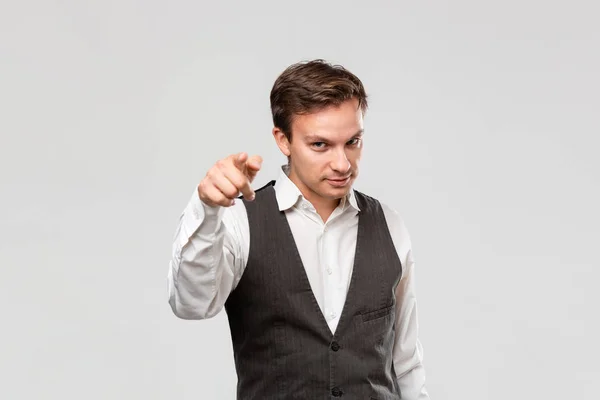 Joven guapo con camisa blanca y chaleco gris apuntando con el dedo a la cámara aislada sobre fondo gris . — Foto de Stock