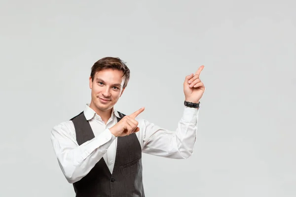 Hombre guapo con camisa blanca y chaleco gris mostrando con los dedos en el espacio vacío para la publicidad en la esquina superior derecha de fondo gris claro . — Foto de Stock