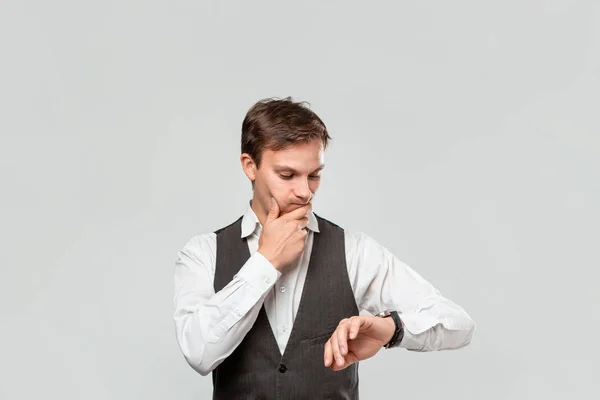Jovem homem de negócios com uma camisa branca e colete cinza verificando o tempo em seu relógio de pulso. Conceito de pontualidade — Fotografia de Stock