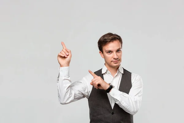 Hombre guapo con camisa blanca y chaleco gris mostrando con los dedos en el espacio vacío para la publicidad en la esquina superior izquierda de fondo gris claro . — Foto de Stock