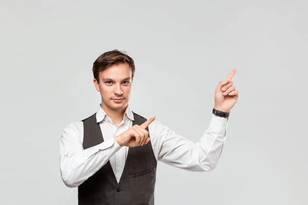 Hombre guapo con camisa blanca y chaleco gris mostrando con los dedos en el espacio vacío para la publicidad en la esquina superior derecha de fondo gris claro . — Foto de Stock
