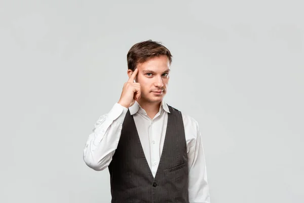 Jovem homem de negócios em uma camisa branca e colete cinza expressando gesto de shinking segurando o dedo perto de sua cabeça . — Fotografia de Stock