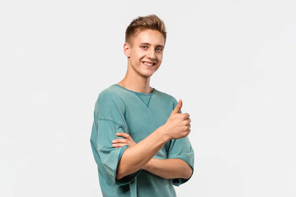 Jovem bonito sorridente com uma t-shirt verde segurando o polegar para cima mostrando sua avaliação. Conceito de como — Fotografia de Stock