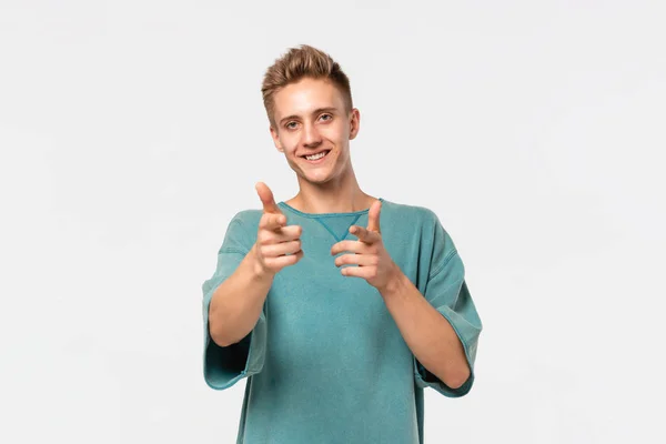 Sorrindo jovem bonito em um tee verde apontando com os dedos para a câmera isolada sobre fundo branco . — Fotografia de Stock