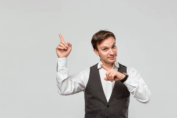 Hombre guapo con camisa blanca y chaleco gris mostrando con los dedos en el espacio vacío para la publicidad en la esquina superior izquierda de fondo gris claro . — Foto de Stock