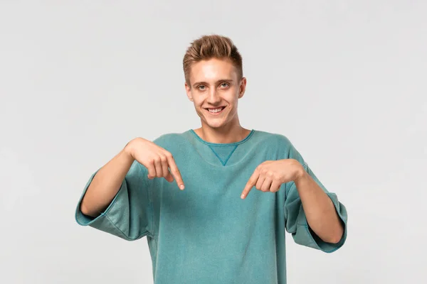 Hezký mladík v zeleném tričku, ukazující prsty dolů na prázdné místo pro reklamu. Místo pro inzerci — Stock fotografie