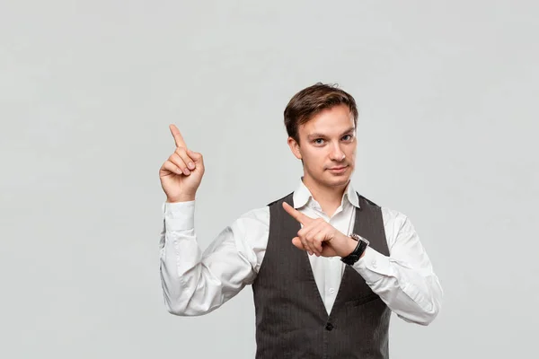 Hombre guapo con camisa blanca y chaleco gris mostrando con los dedos en el espacio vacío para la publicidad en la esquina superior izquierda de fondo gris claro. Lugar para la publicidad — Foto de Stock