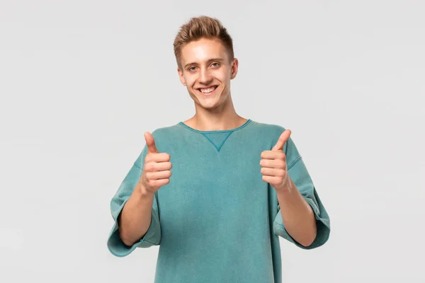 Uśmiechnięty, przystojny młodzieniec w zielonej koszulce z kciukiem do góry, pokazujący swoją ocenę. Koncepcja podobna — Zdjęcie stockowe