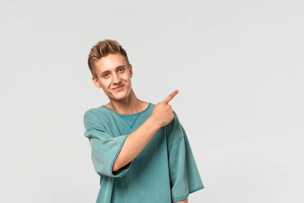 녹색 티를 입은 잘생긴 청년, 흰 배경의 오른쪽에 있는 광고를 위한 빈자리에 손가락을 보이고 있는 모습. — 스톡 사진