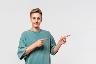 Yeşil tişörtlü yakışıklı genç adam, parmaklarıyla reklam için boş alanı gösteriyor..