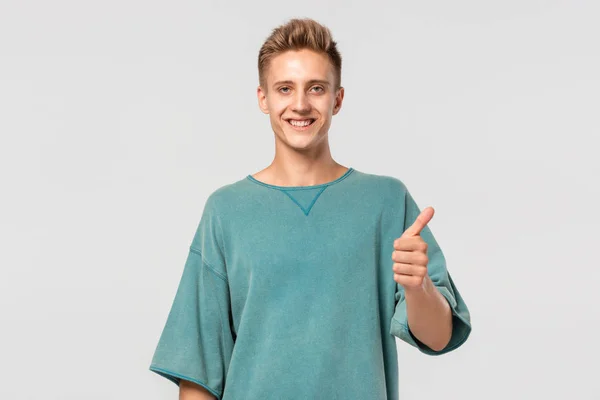 Leende stilig ung man i grön t-shirt håller tummen upp visar sin utvärdering. — Stockfoto