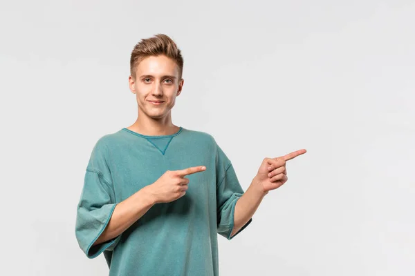 Stilig ung man i en grön tee visar med fingrarna precis vid det tomma utrymmet för reklam. — Stockfoto