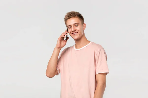 Ganska blond tonåring i en rosa t-shirt leende talar i telefon. — Stockfoto