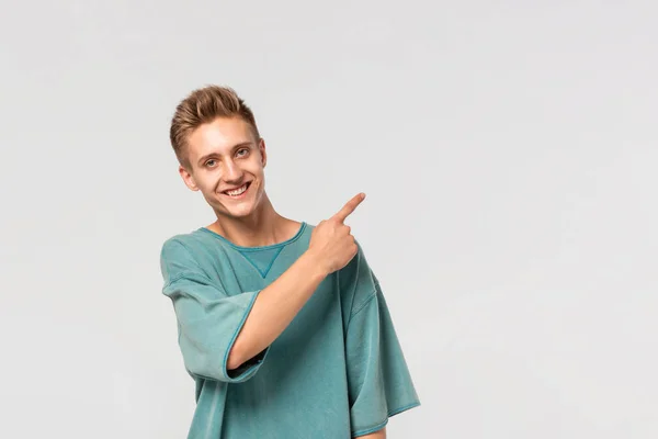 Jóképű fiatalember zöld pólóban, az ujjával mutatja az üres reklámfelületet.. — Stock Fotó