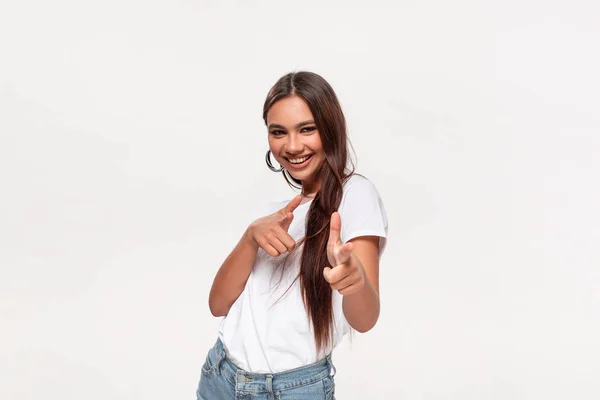 Excited pretty african-american teenager in a white t-shirt and blue jeans holding fingers in a finger gun gesture.
