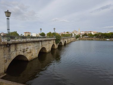 The historic granite Old Bridge crosses the Tua River in Mirandela, Portugal, with the cityscape and iconic tower behind. This scenic pedestrian landmark blends heritage and beauty in northern Portugal.