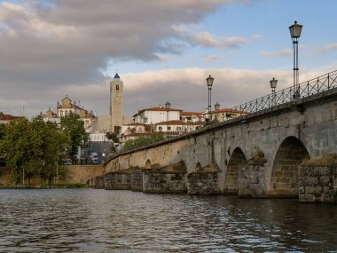 The historic granite Old Bridge crosses the Tua River in Mirandela, Portugal, with the cityscape and iconic tower behind. This scenic pedestrian landmark blends heritage and beauty in northern Portugal.